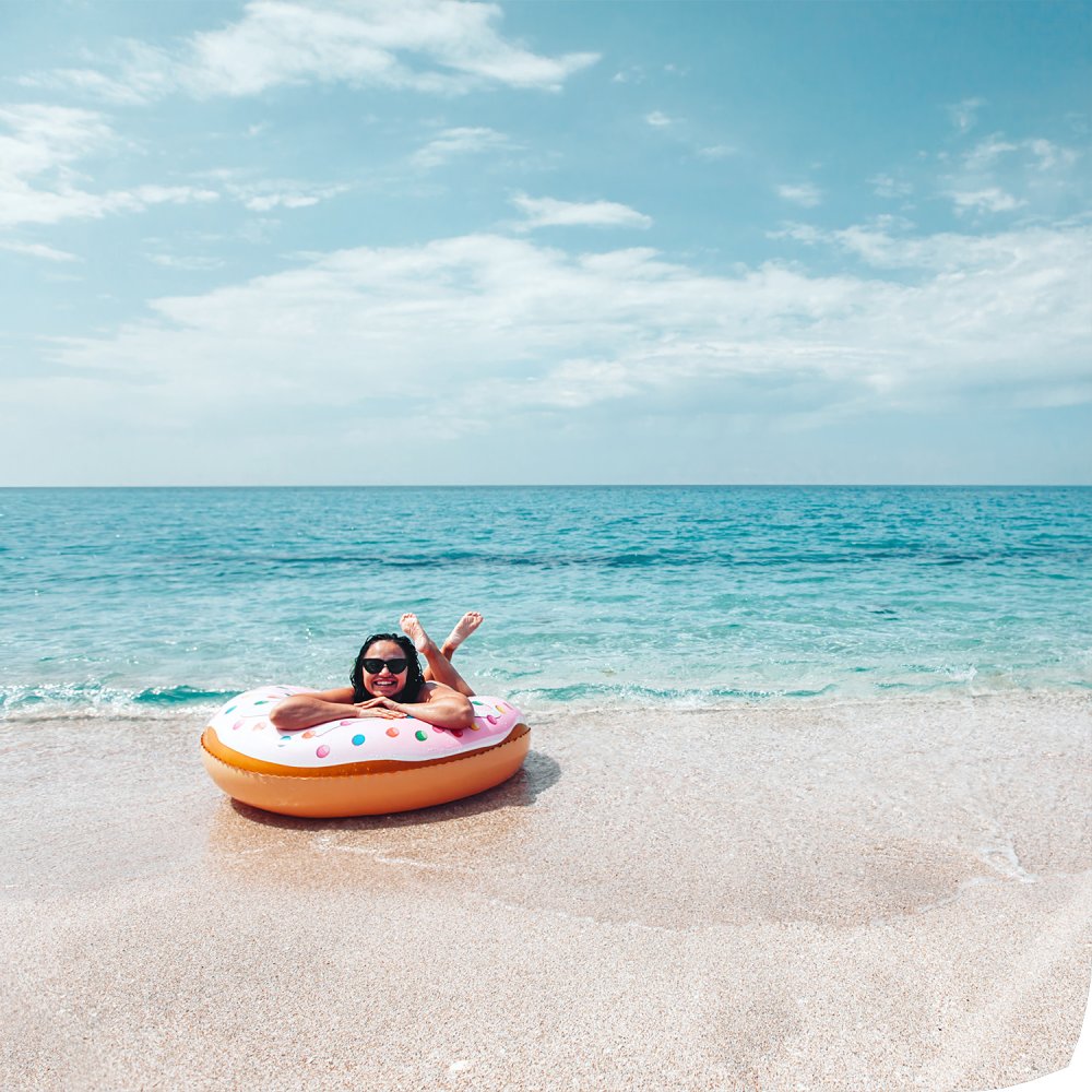 Premium Poster 20x20 cm Quadrat matt zeigt Frau mit Sonnenbrille entspannt auf einem aufblasbaren Donut am Strand im Meer.