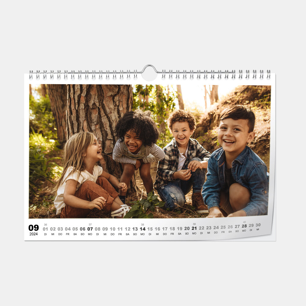 Der Digitaldruck-Fotokalender im A4-Querformat zeigt vier fröhlich lachende Kinder spielend im Wald vor einem Baum.