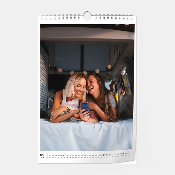 Digitaldruck Fotokalender A4 Hochformat mit Hochglanz-Oberfläche zeigt zwei lachende Frauen, die auf ein Handy schauen.